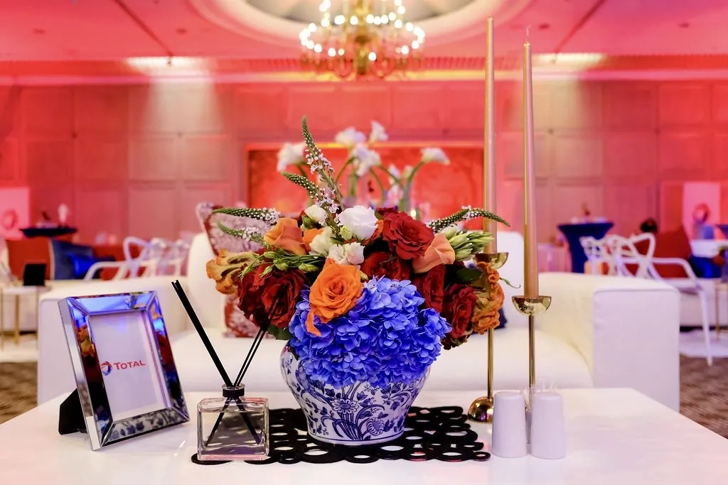 Corporate event centrepiece of blue hydrangeas and roses in a patterned ceramic vase, with lounge seating beyond